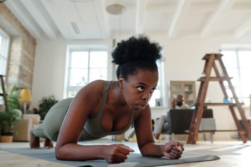 Fit young African woman in activewear doing plank on mat on the floor of living-room